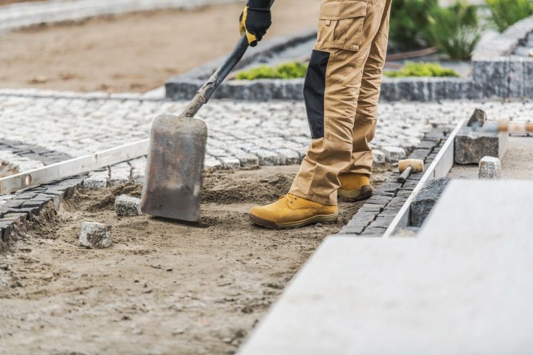 Construction Worker Laying Stone Pavers in Garden Pathway During Daytime in Residential Area